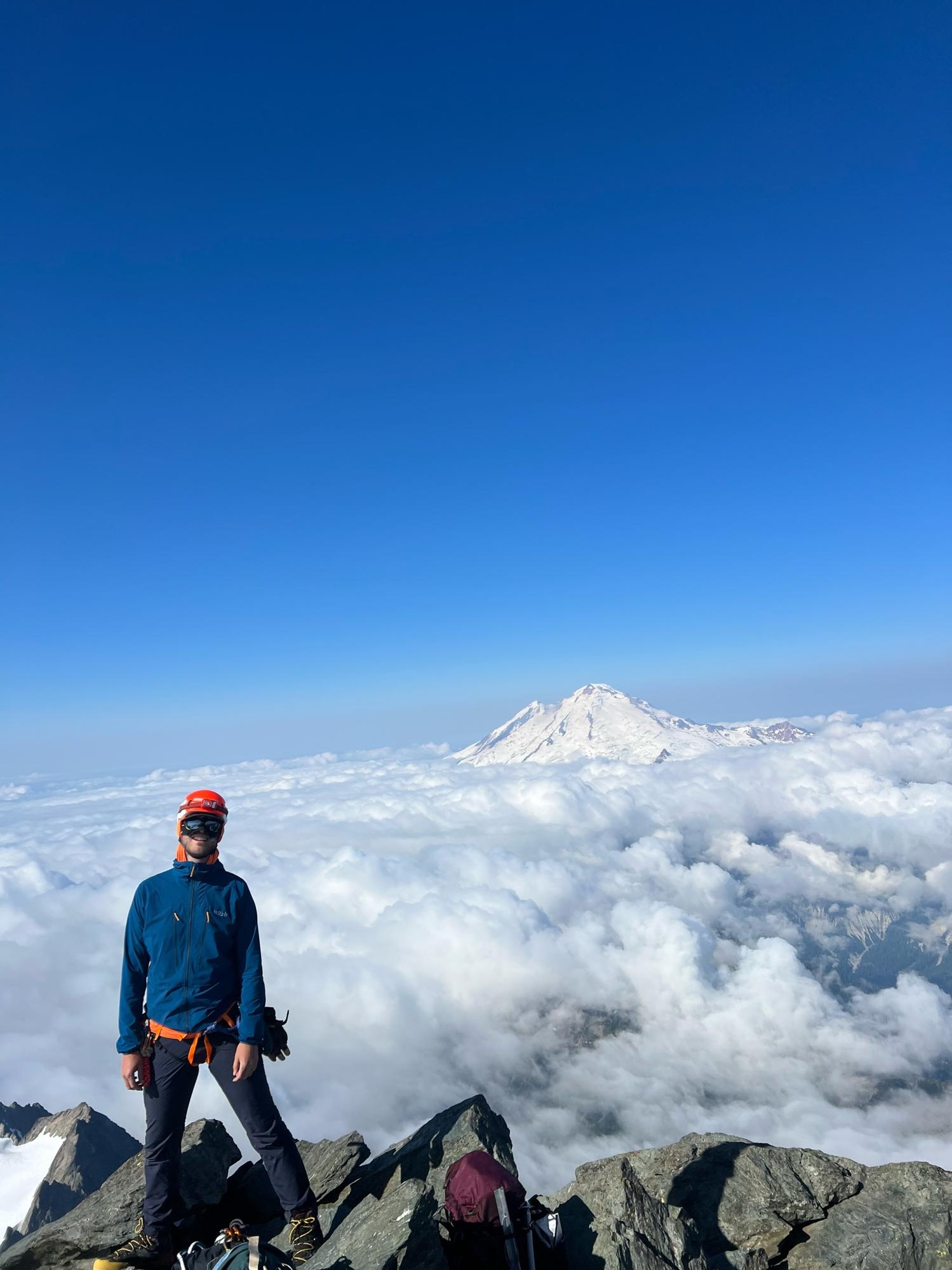 Standing on a summit above a layer of clouds with a distant volcano