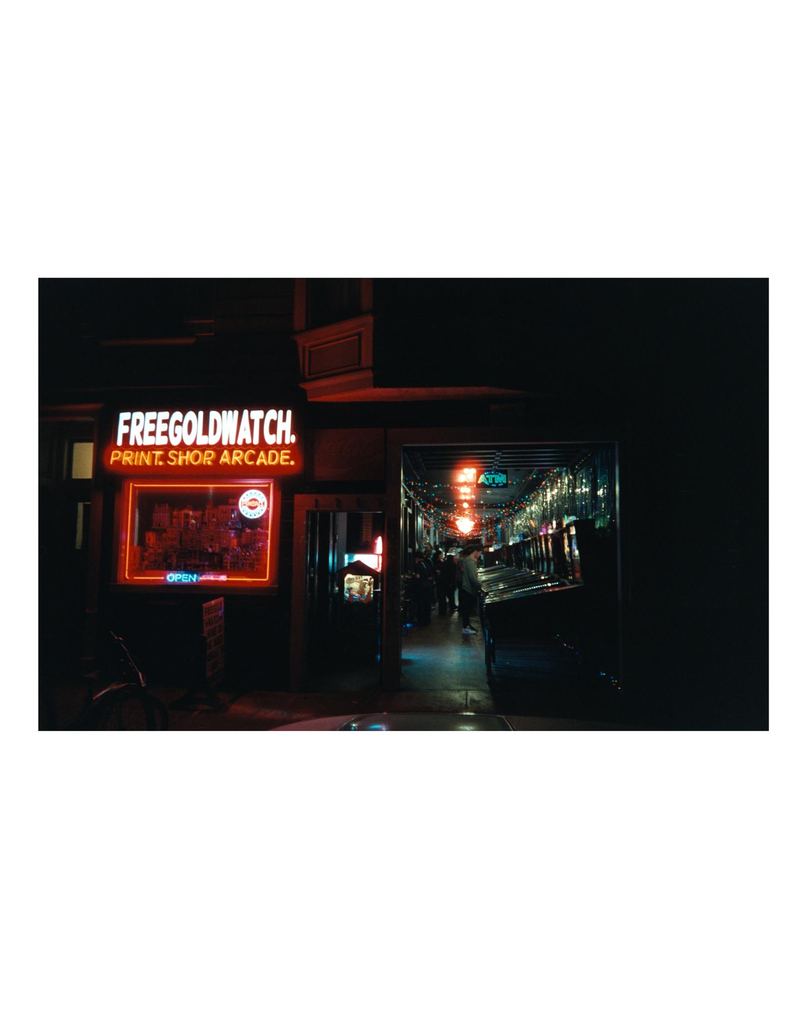 The red neon sign of Free Gold Watch print shop and pinball arcade at night
